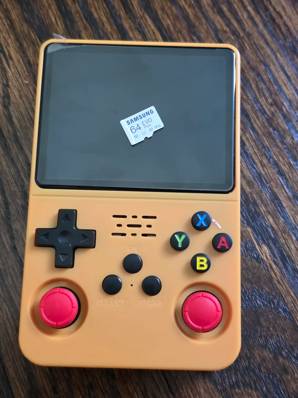 The R36S lying face up on a wooden table with its microSD card resting on the dark screen.
